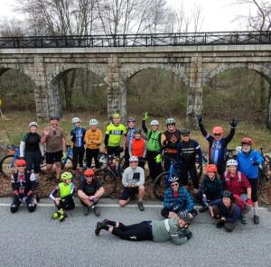 Group of riders in front of the Holliston rail trail bridge.